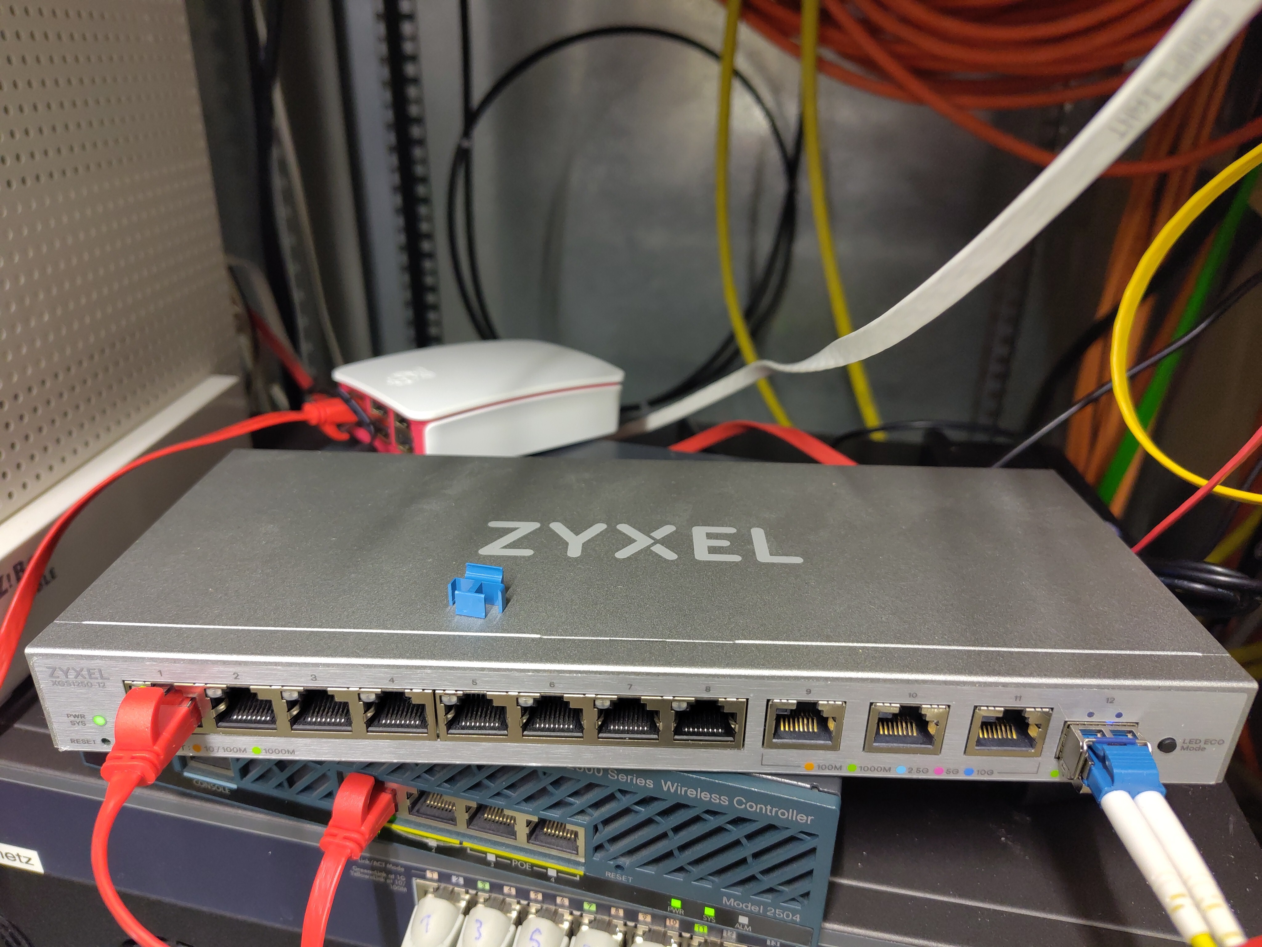 Front of the Zyxel XGS1250-12 network switch, showing a connected SFP+ fiber module and one connected ethernet port